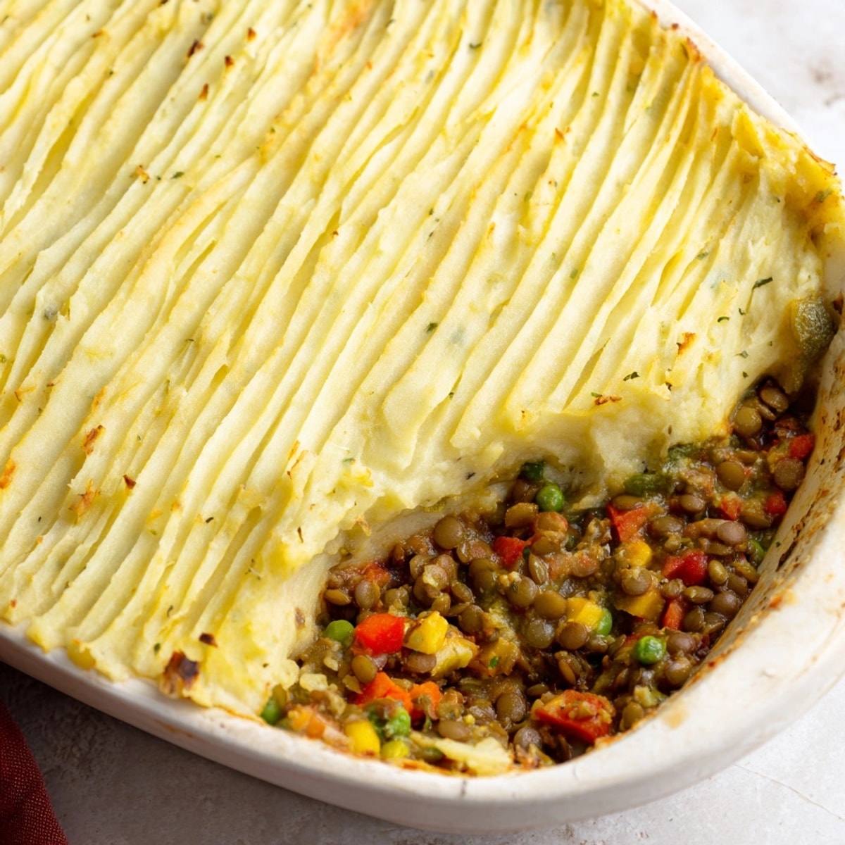 Hearty Lentil &amp; Veggie Shepherds Pie filling bubbling, topped with fluffy mashed potatoes.