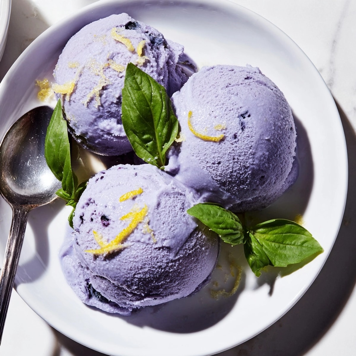 Close-up of homemade Blueberry & Basil Lemonade Sorbet, swirled in a glass dessert bowl, glistening.