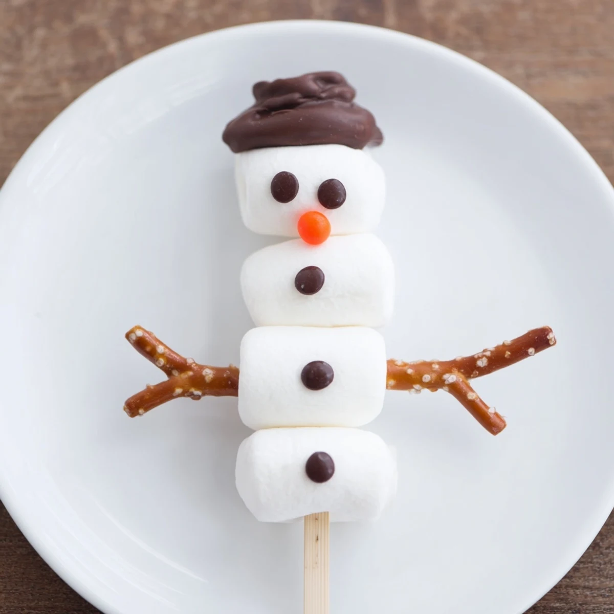 Marshmallow snowman stick arrangement: a festive dessert of white marshmallow snowmen on wooden sticks.
