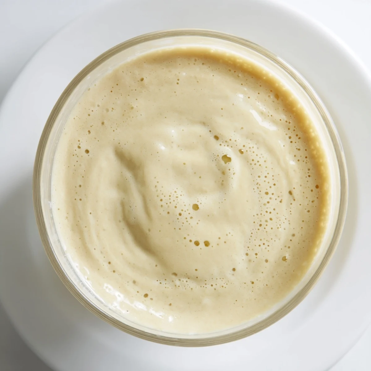 This vibrant banana smoothie showcases a thick, creamy texture with flecks of ice, a refreshing treat.