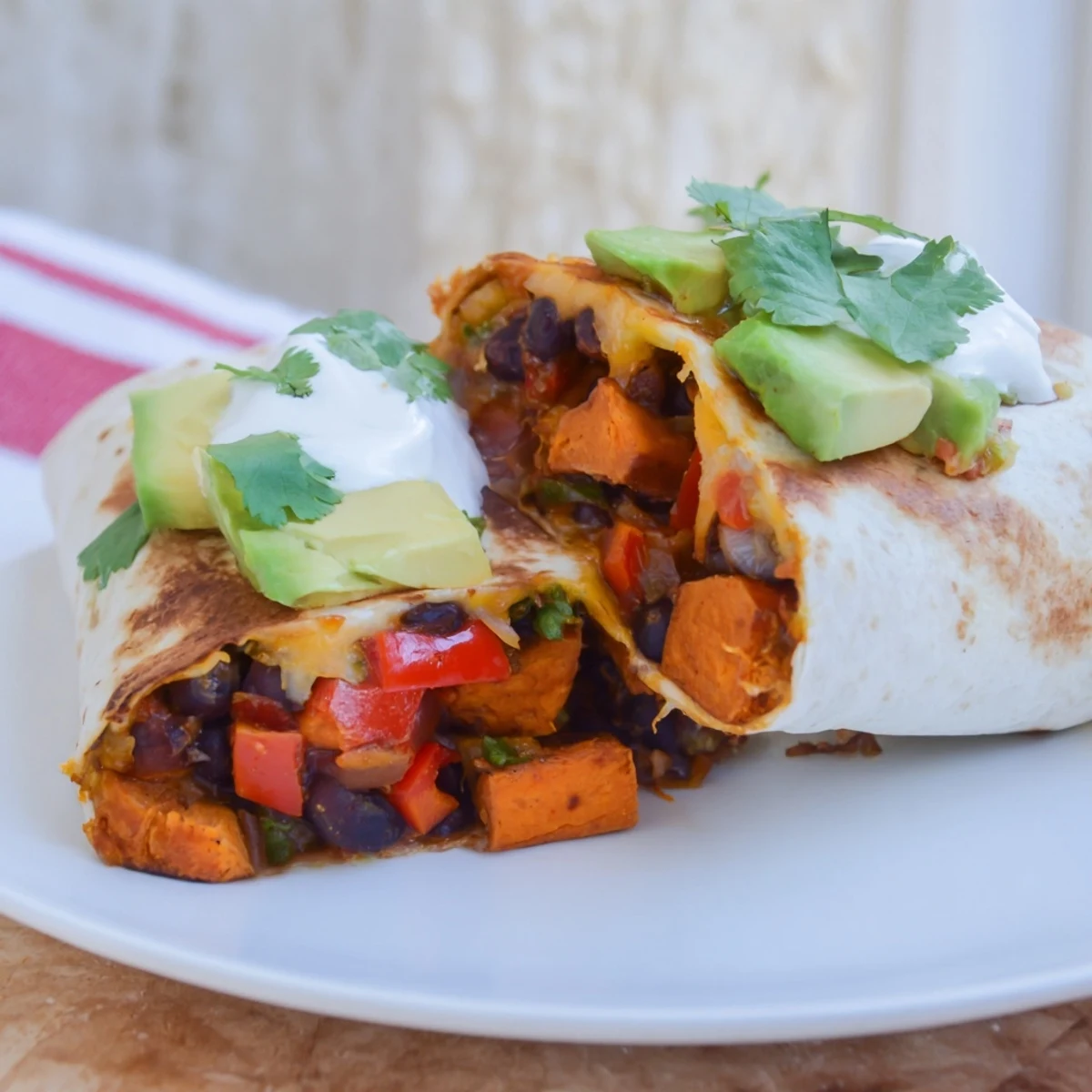 Golden roasted sweet potato and black bean burritos filled with spicy vegetables and fresh cilantro on a plate.
