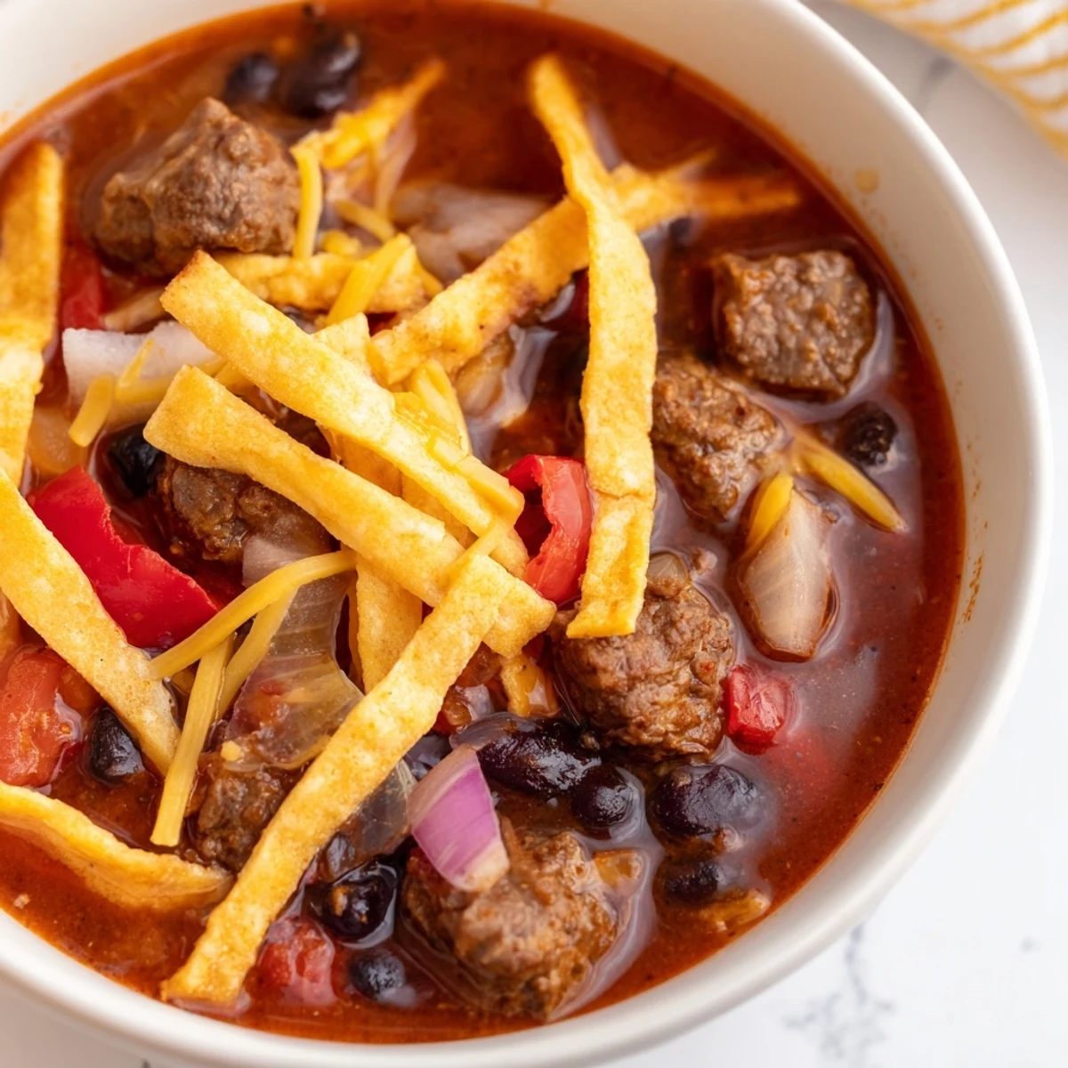 Spicy Beef Enchilada Soup served with crunchy tortilla strips and lime wedges on a rustic table setting.