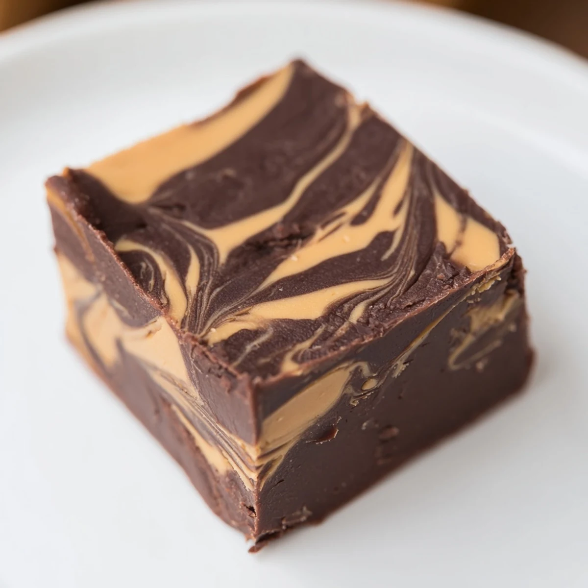 Chocolate Peanut Butter Fudge Squares stacked neatly on a small plate, drizzled with melted peanut butter for an extra sweet finish.
