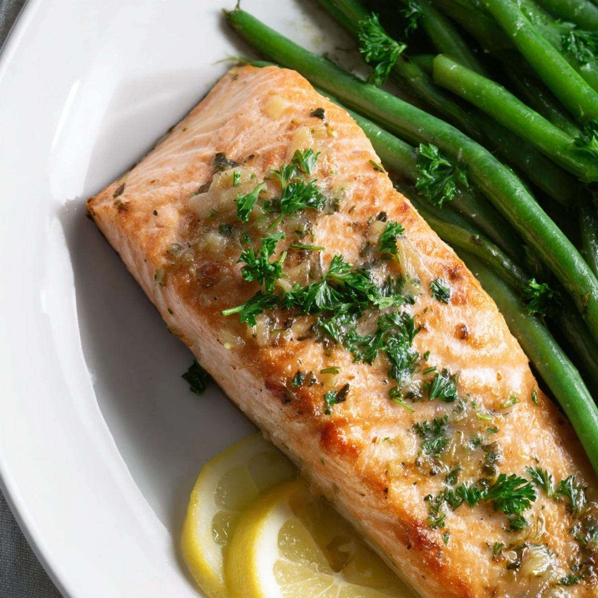 Tender flaky salmon fillets paired with crisp green beans, garnished with fresh parsley and lemon wedges.