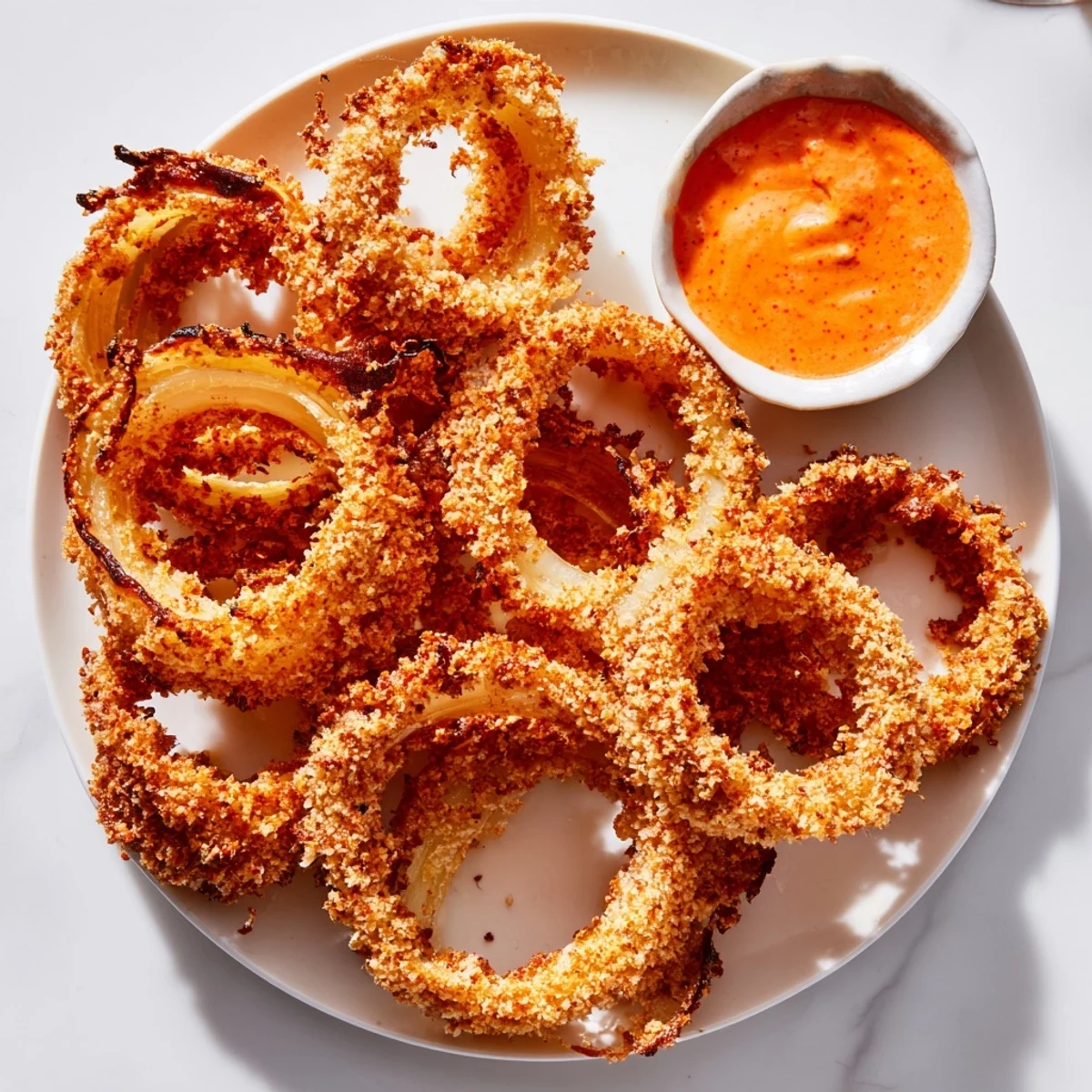 Crispy onion rings stacked high with golden crumbs, served alongside a vibrant orange spicy mayo dip.