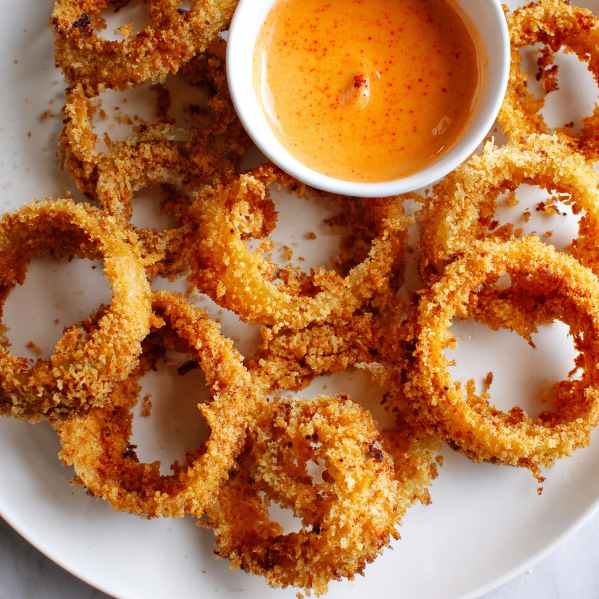Deep-fried Crispy Onion Rings with Spicy Mayo Dipping Sauce, glistening with oil on a plate.