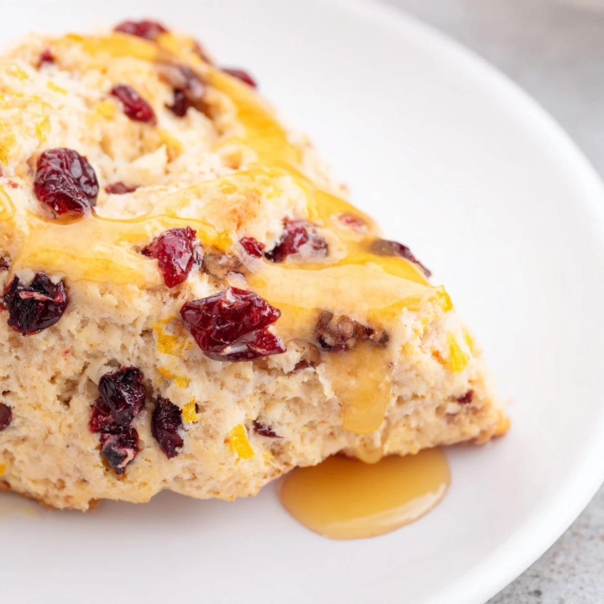 A close-up of a split Cranberry Orange Scone revealing buttery layers, sweet citrus glaze, and a side of steaming coffee for an afternoon snack.