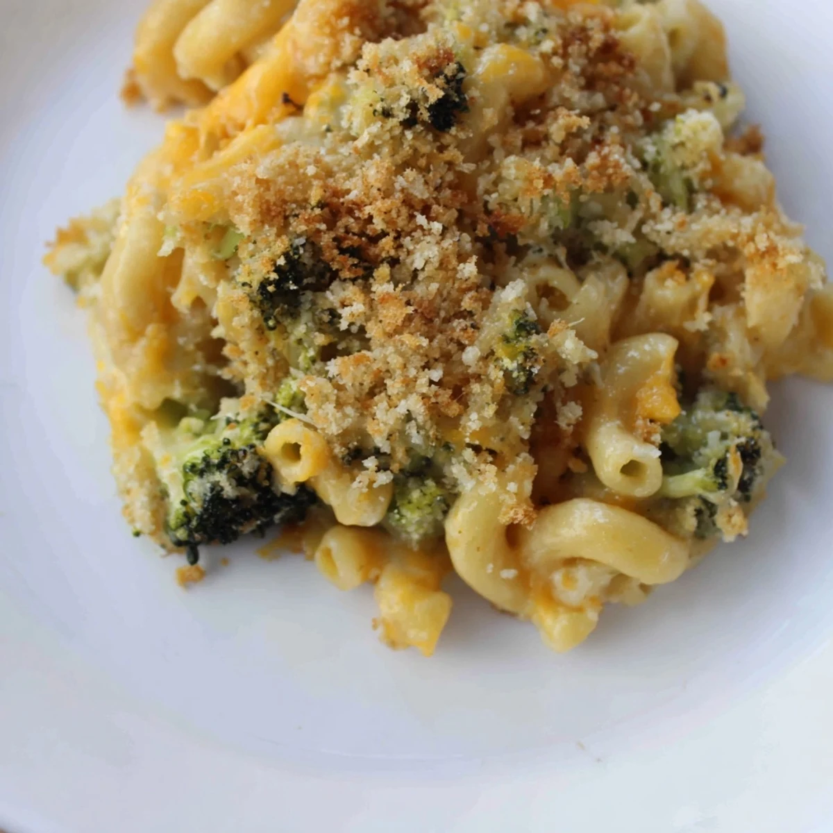 Golden baked macaroni and cheese with broccoli in a casserole dish, featuring tender pasta and a crunchy breadcrumb topping.