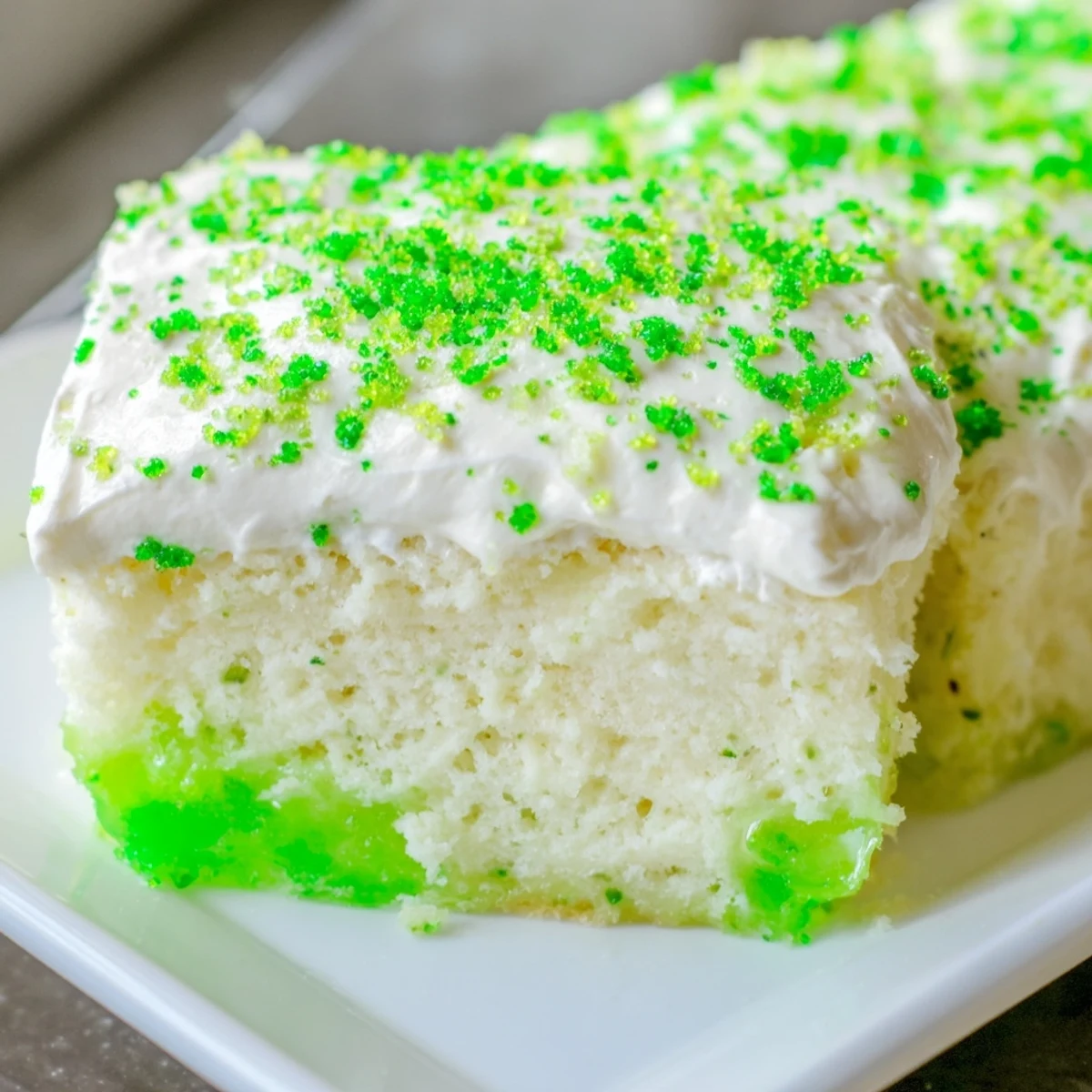 Freshly baked St. Patrick's Day Lime Poke Cake showcases vibrant green gelatin soaking into moist white cake before creamy topping is spread.
