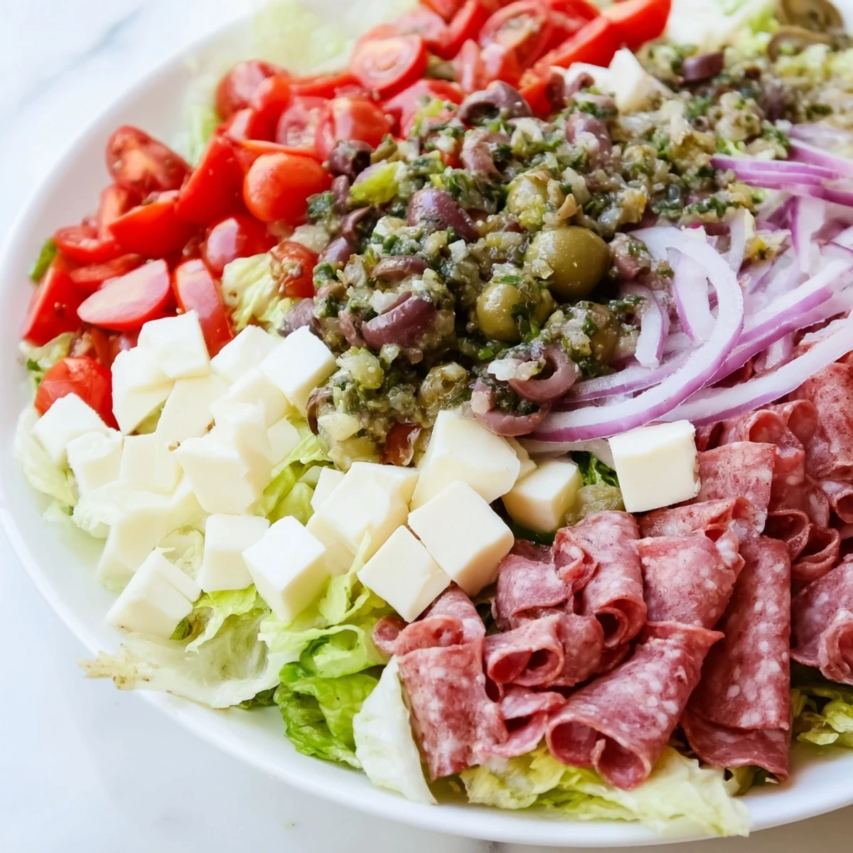 Hearty New Orleans Muffuletta Salad with cured meats, cubed cheeses, and a zesty olive relish on romaine.