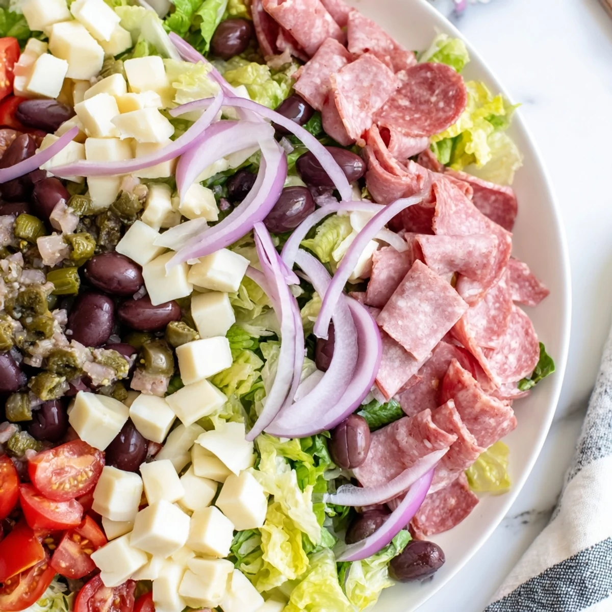 Vibrant New Orleans Muffuletta Salad in a white bowl, topped with salami, mozzarella, and olive relish.