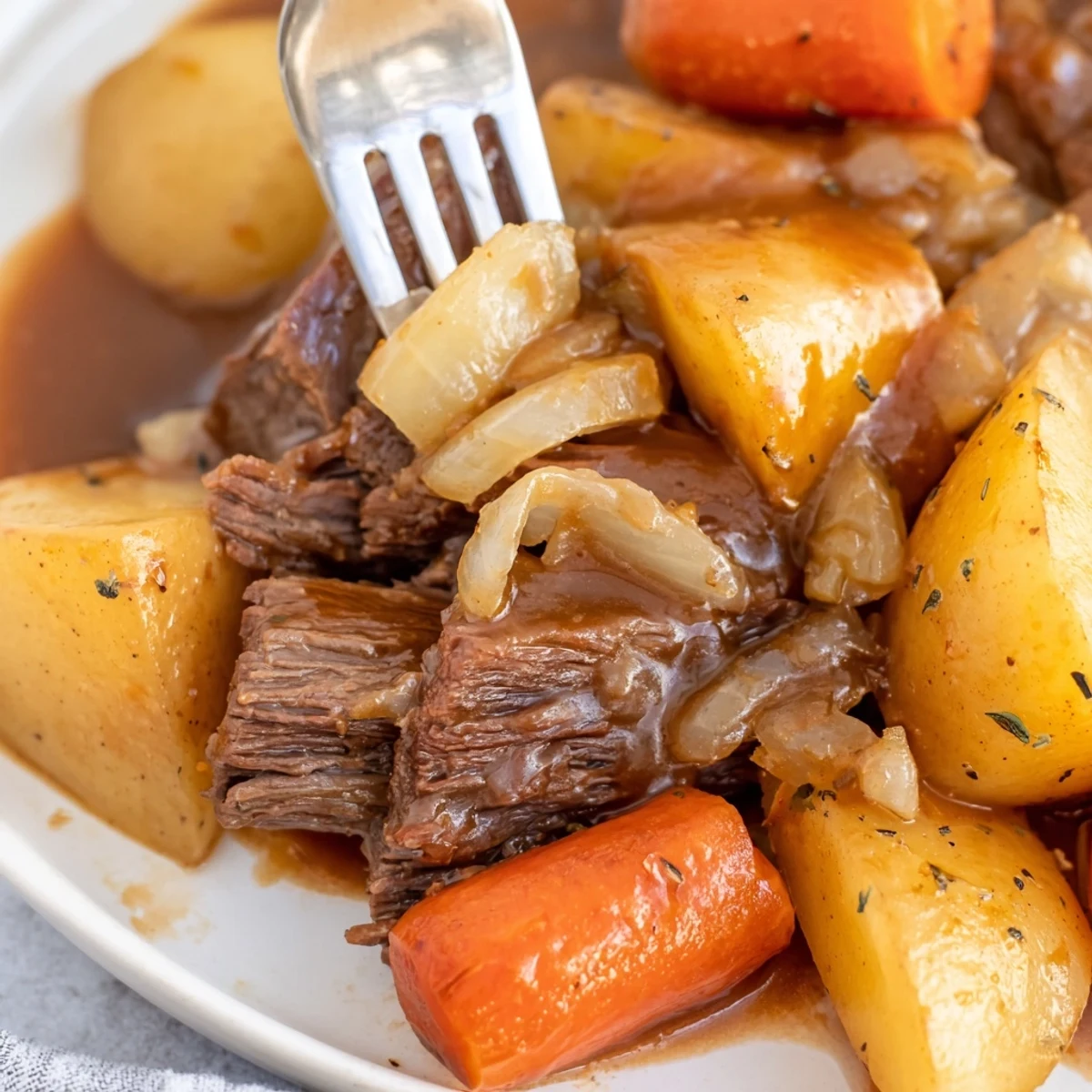 Fork-tender Irish Beef Pot Roast surrounded by caramelized carrots and potatoes, drizzled with thick, glossy gravy.