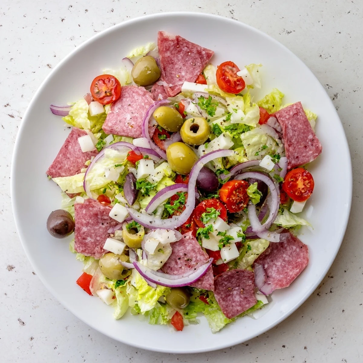 A plated New Orleans Muffuletta Salad features crisp lettuce, cherry tomatoes, and marinated olive mix, ready to serve.