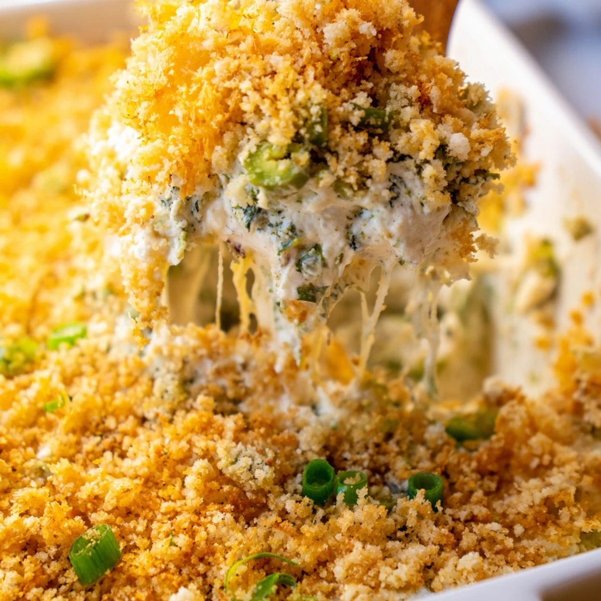 Freshly baked Jalapeno Popper Dip in a ceramic dish, garnished with green onions and jalapeno slices alongside a sliced baguette.