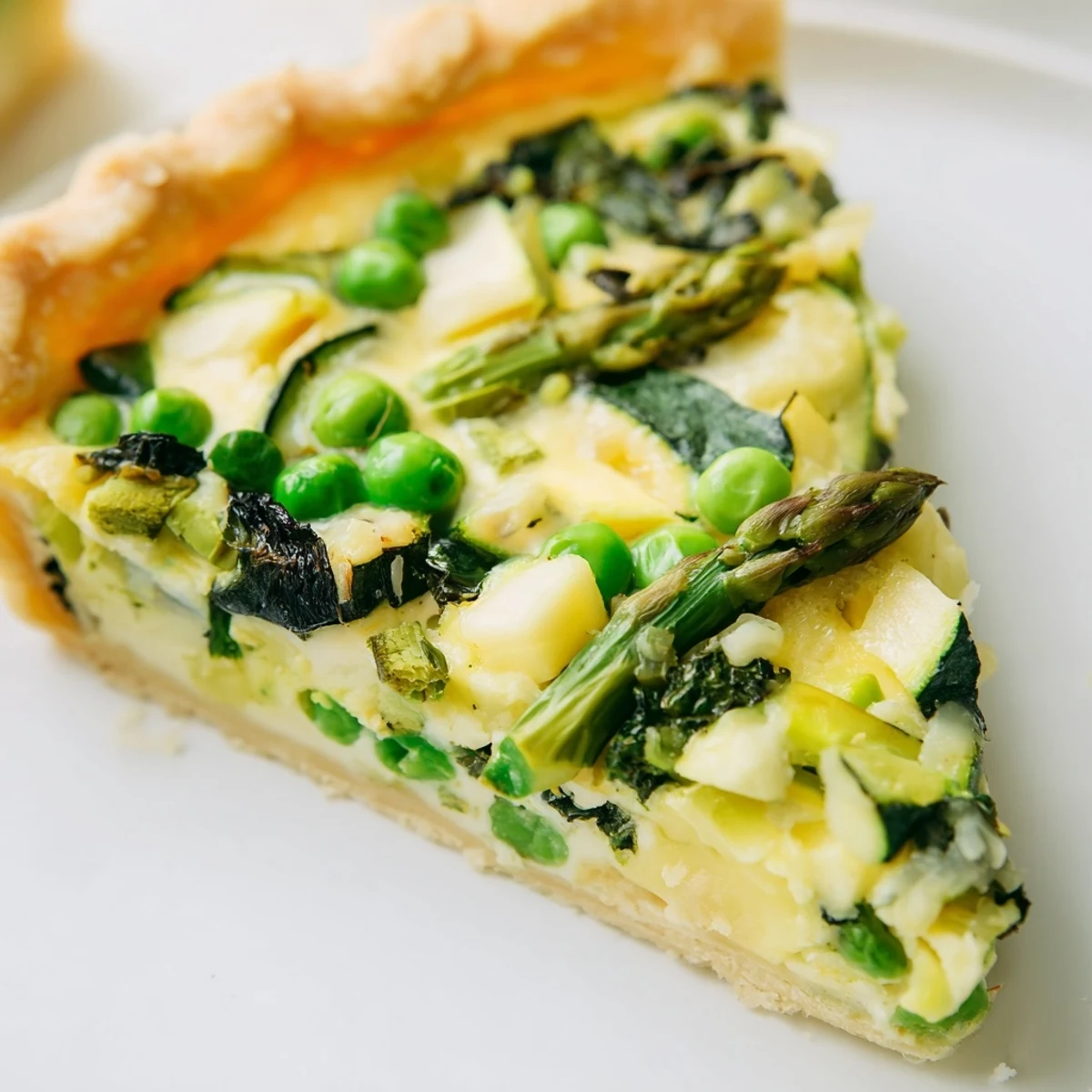 Slice of warm Spring Vegetable Quiche on a rustic plate, revealing layers of spinach, scallions, and melted Gruyère cheese for a savory brunch.  