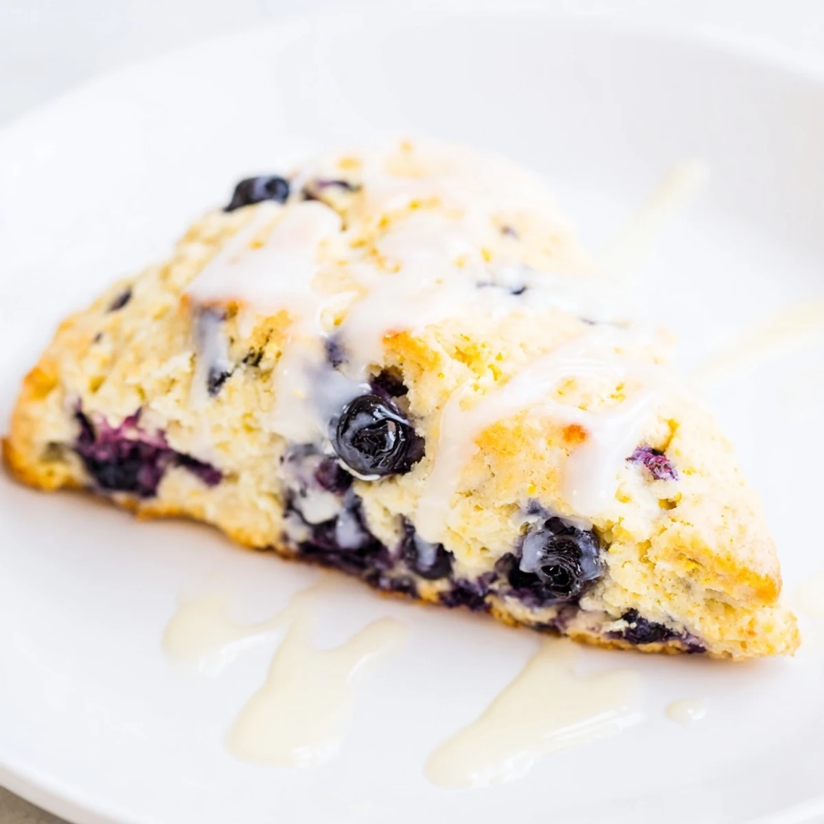 Lemon Blueberry Scones with Vanilla Glaze arranged on a white plate with a glass of milk for serving.