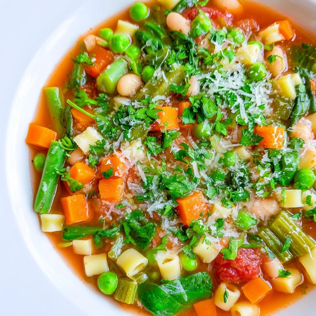Spoon dipping into a hearty Spring Vegetable Minestrone Soup garnished with fresh parsley and grated Parmesan cheese.