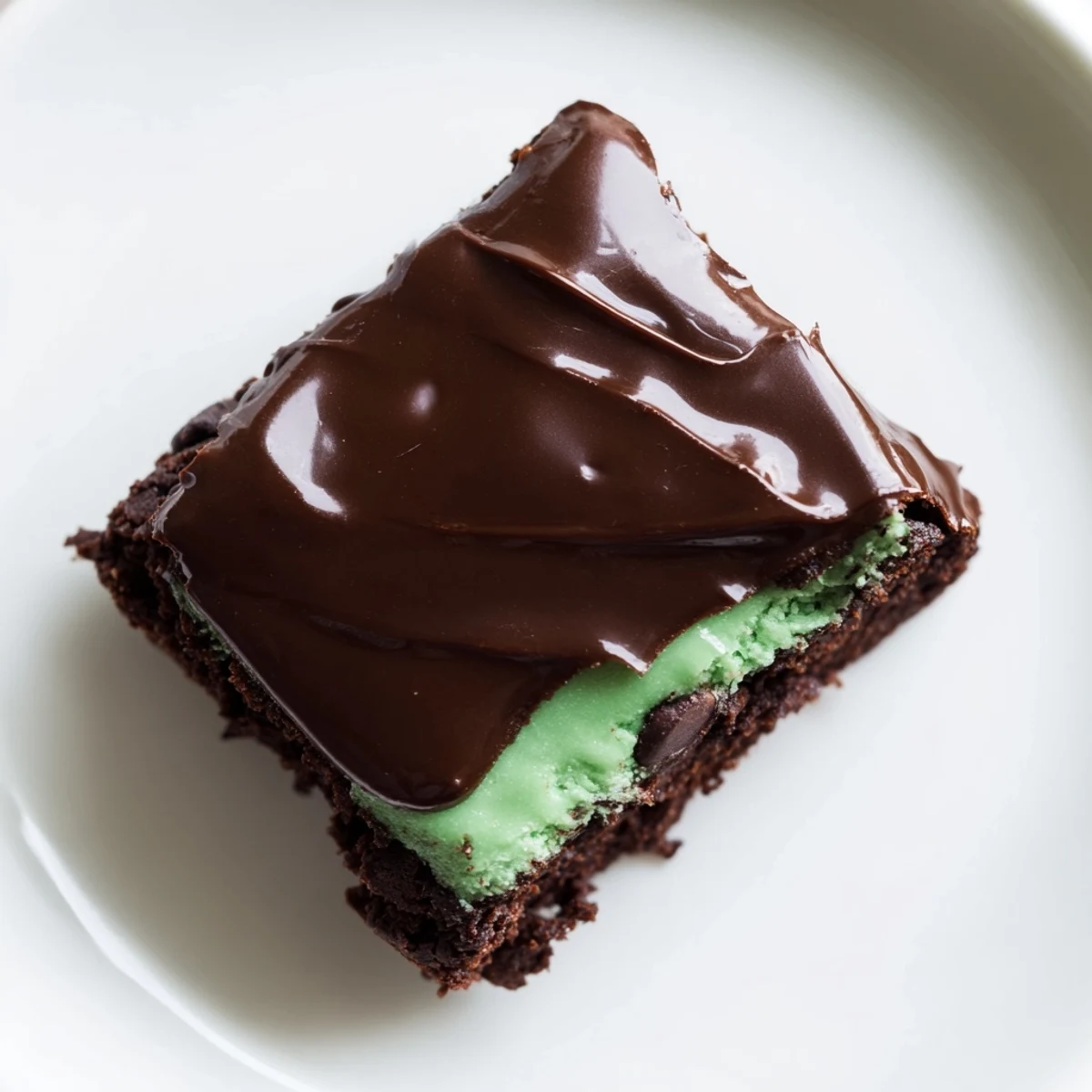 A close-up of Mint Chocolate Chip Brownies with a glossy chocolate topping, showing fudgy layers and minty green filling for a dessert lover’s dream.