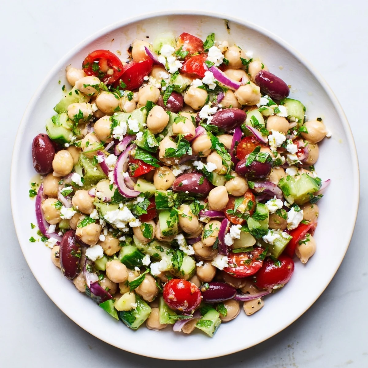 In a white bowl, the Mediterranean Dense Bean Salad is tossed with herbs, olives, and a lemony vinaigrette.