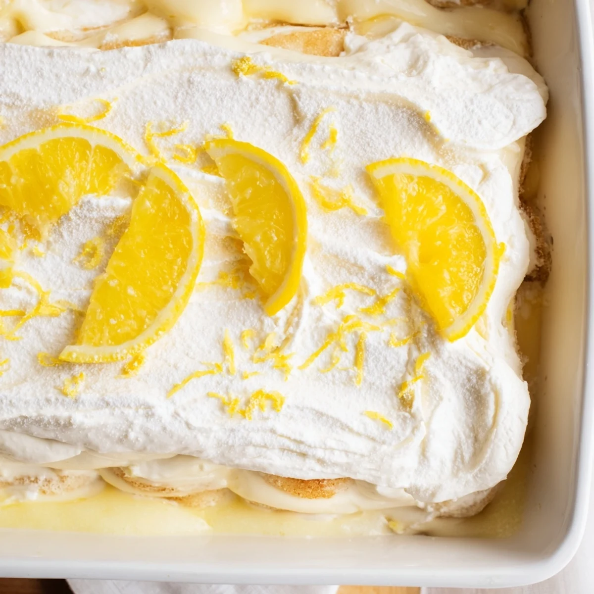 The Easy Lemon Tiramisu No Bake Dessert sits in a glass dish with a fresh lemon wedge garnish, ready for a summer party.