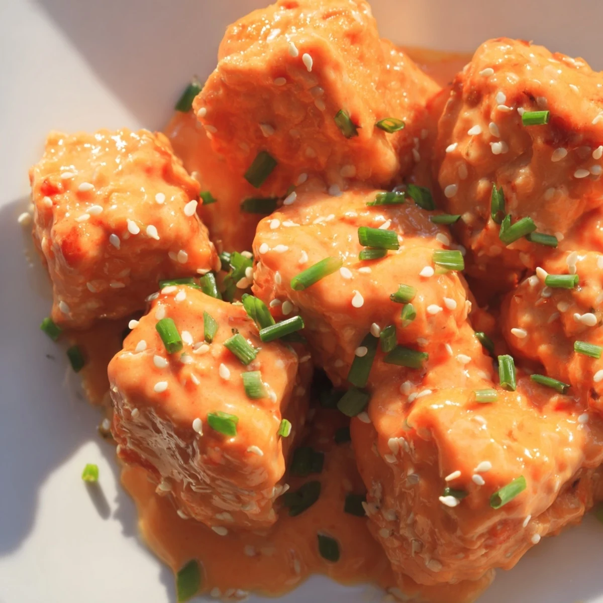 Close-up of tender Bang Bang Salmon Bites coated in spicy orange sauce on a dark serving platter.