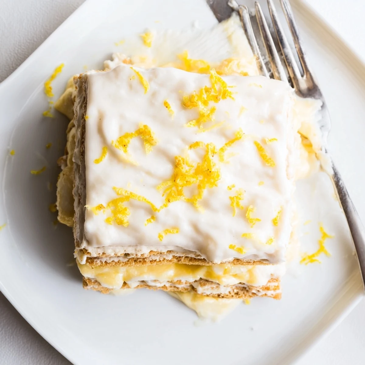A chilled square of No Bake Lemon Eclair Cake topped with zesty glaze and fresh raspberries on a rustic table.