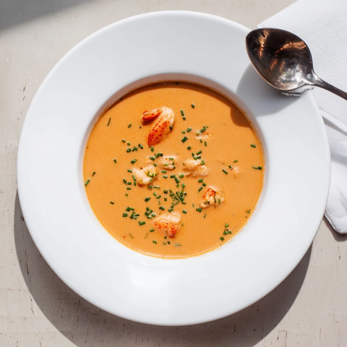 Creamy lobster bisque in a white bowl garnished with fresh chives and tender lobster pieces