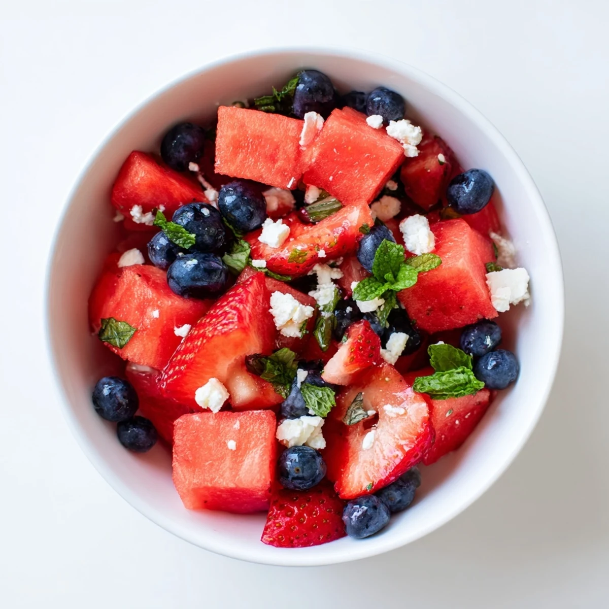 Colorful summer fruit salad featuring strawberries and watermelon cubes coated in zesty honey lime vinaigrette.