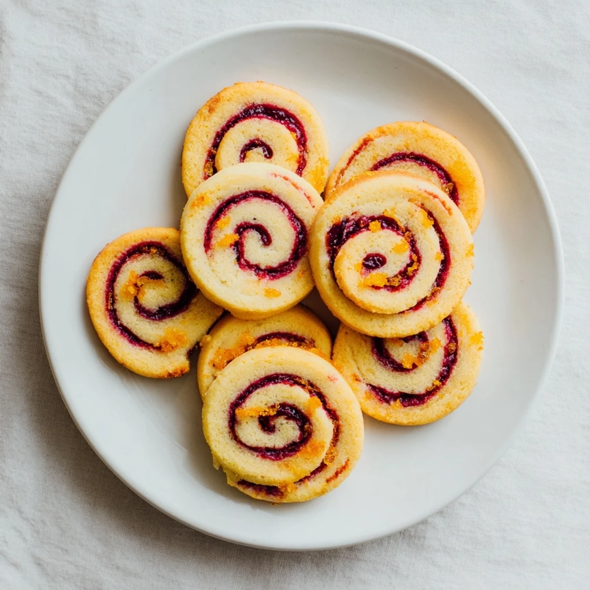 Close up of orange cranberry pinwheel cookies with delicate citrus flecks throughout golden pastry