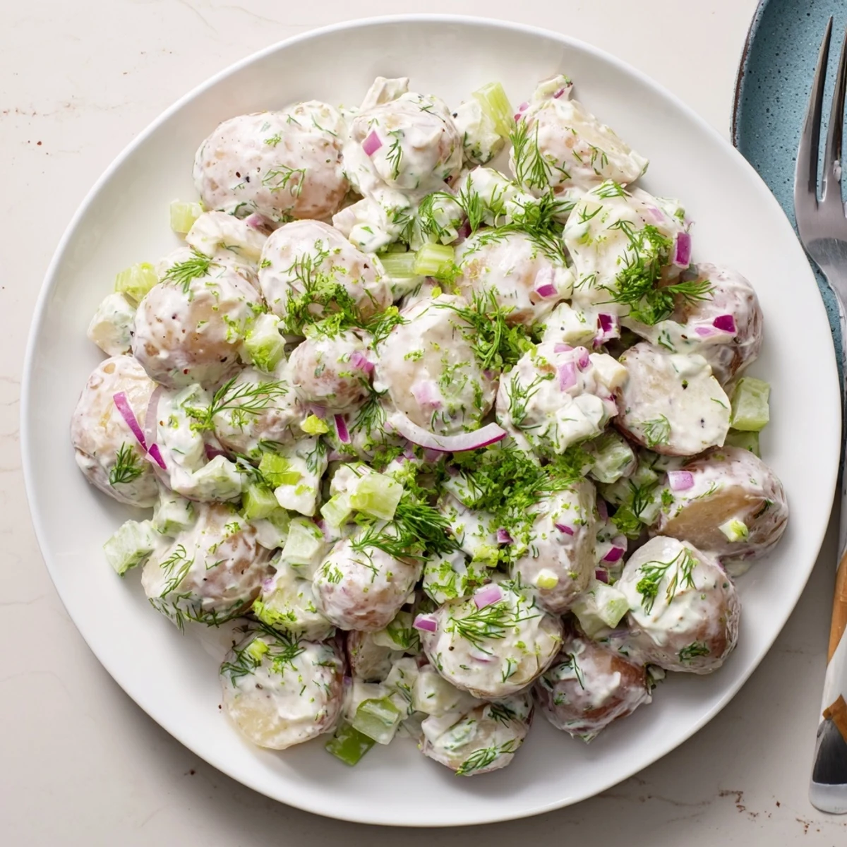 Creamy Greek yogurt potato salad topped with fresh dill and red onion in a serving bowl