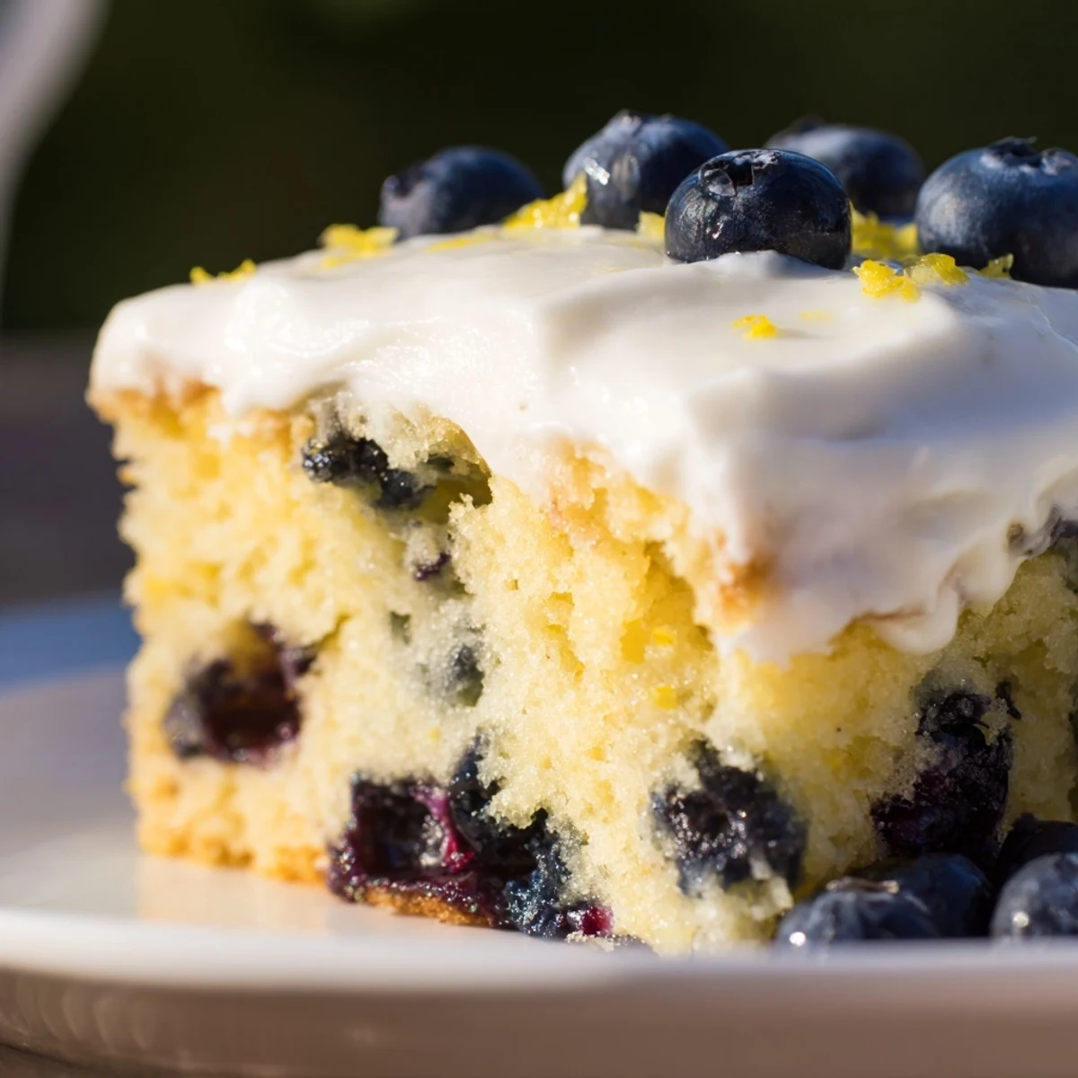 Slice of moist lemon blueberry cake topped with creamy frosting and blueberries