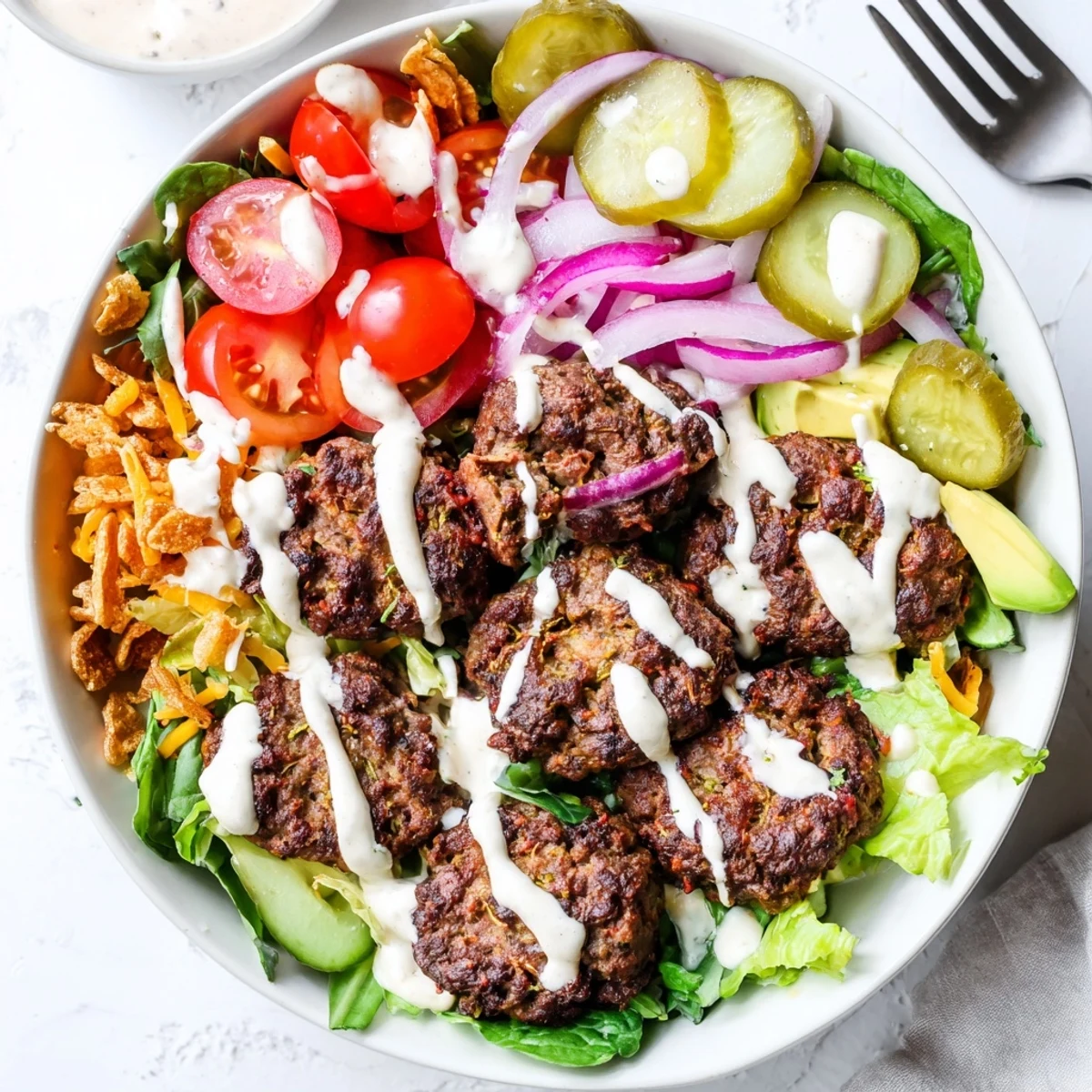 Drizzled smash sauce covers deconstructed smash burger bowl with pickles and cheddar cheese