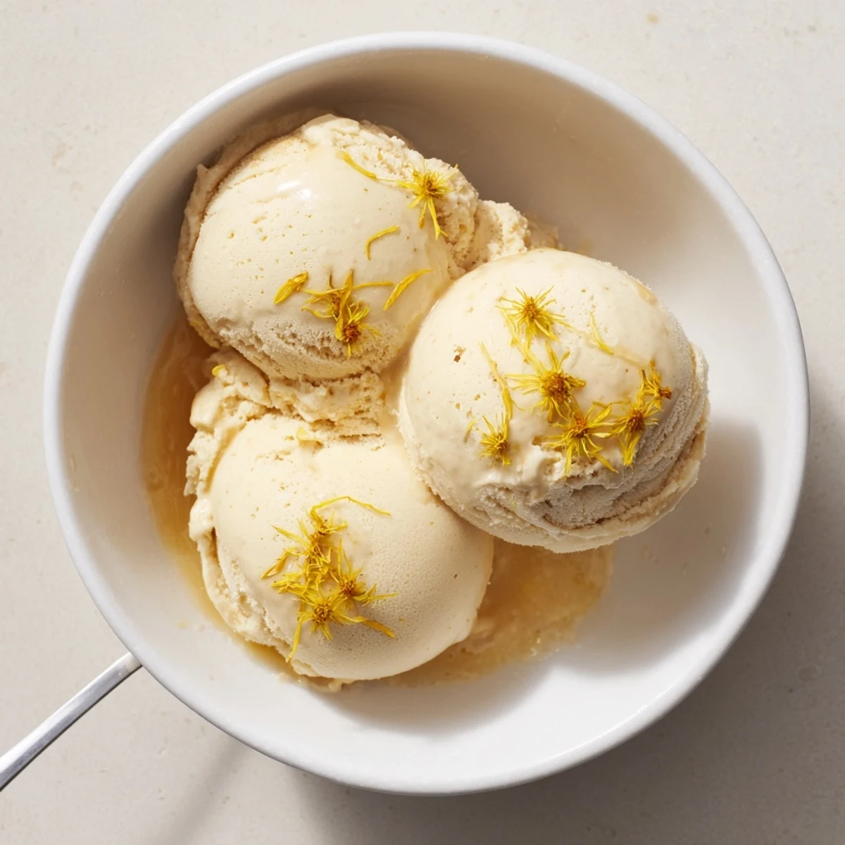 Creamy scoops of dandelion honey ice cream topped with golden petals in a bowl.