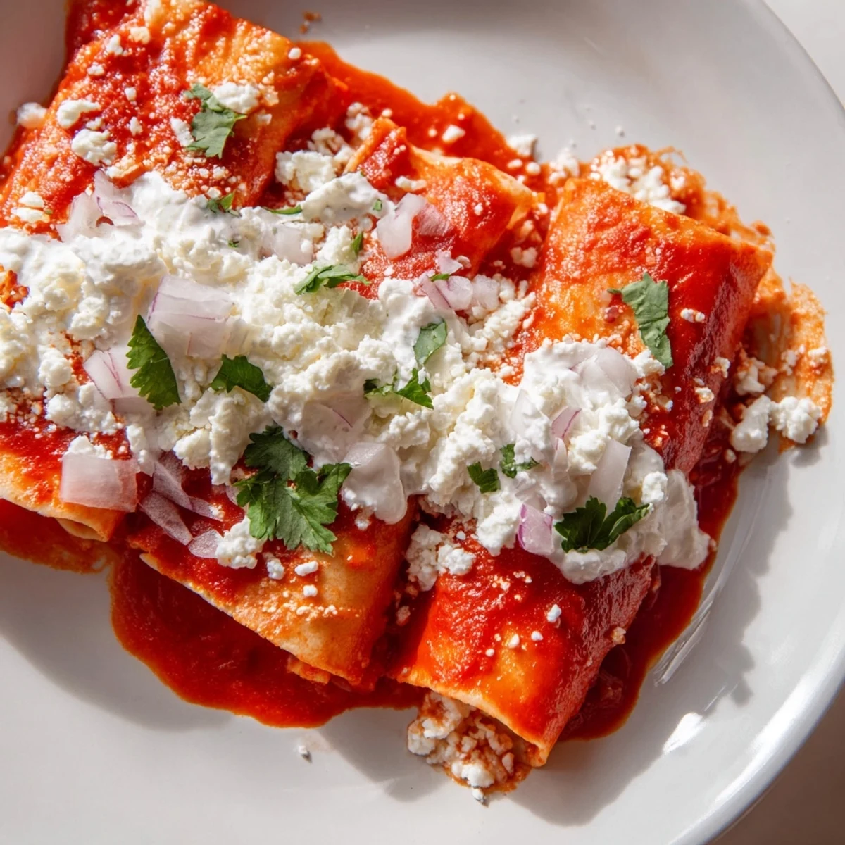 Golden entomatadas draped in rich red tomato sauce topped with crumbled queso fresco and crema