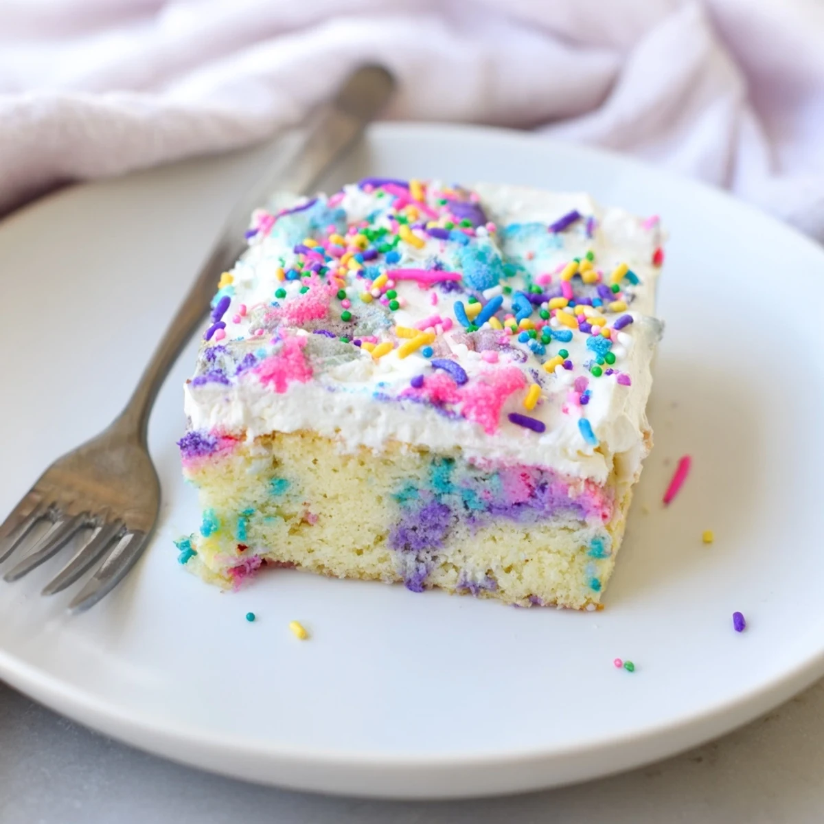 A close-up of unicorn poke cake showing bright pink purple and blue pudding filling