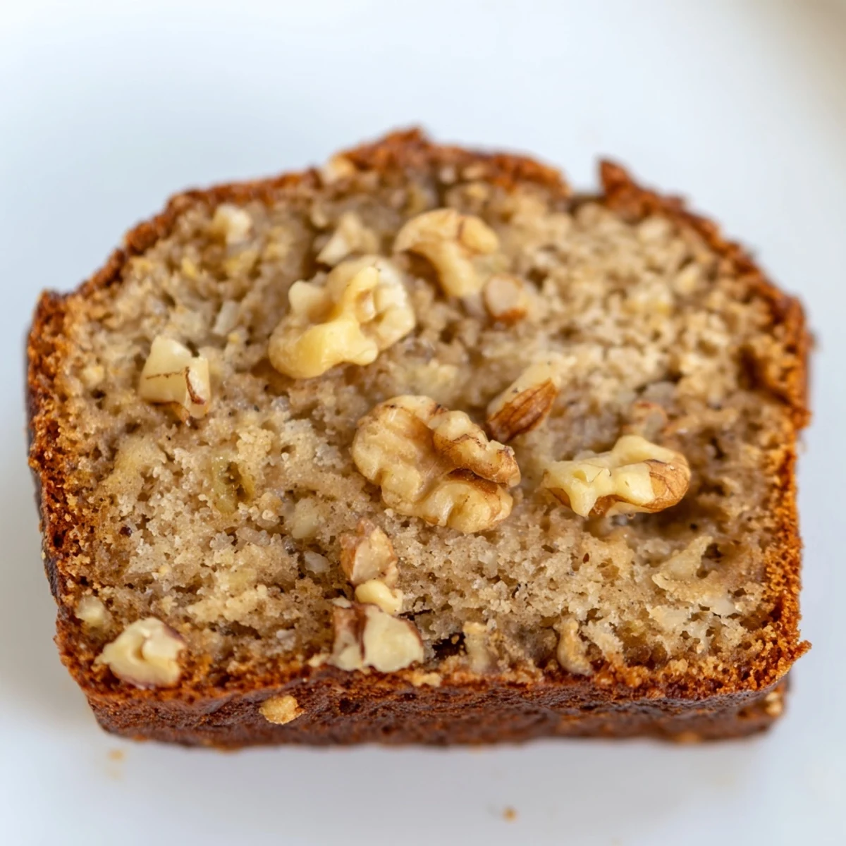 Golden banana nut bread loaf sliced on a rustic cutting board with scattered walnuts