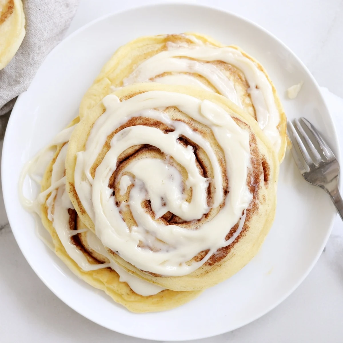 A stack of cinnamon roll pancakes dripping with sweet cream cheese glaze