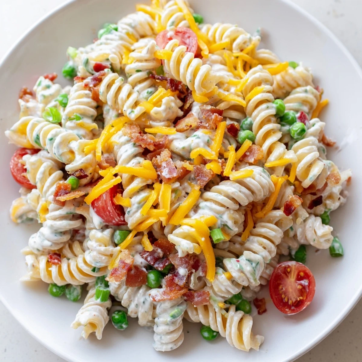 Chilled addictive crack pasta salad on a white plate loaded with green onions peas and gooey cheese