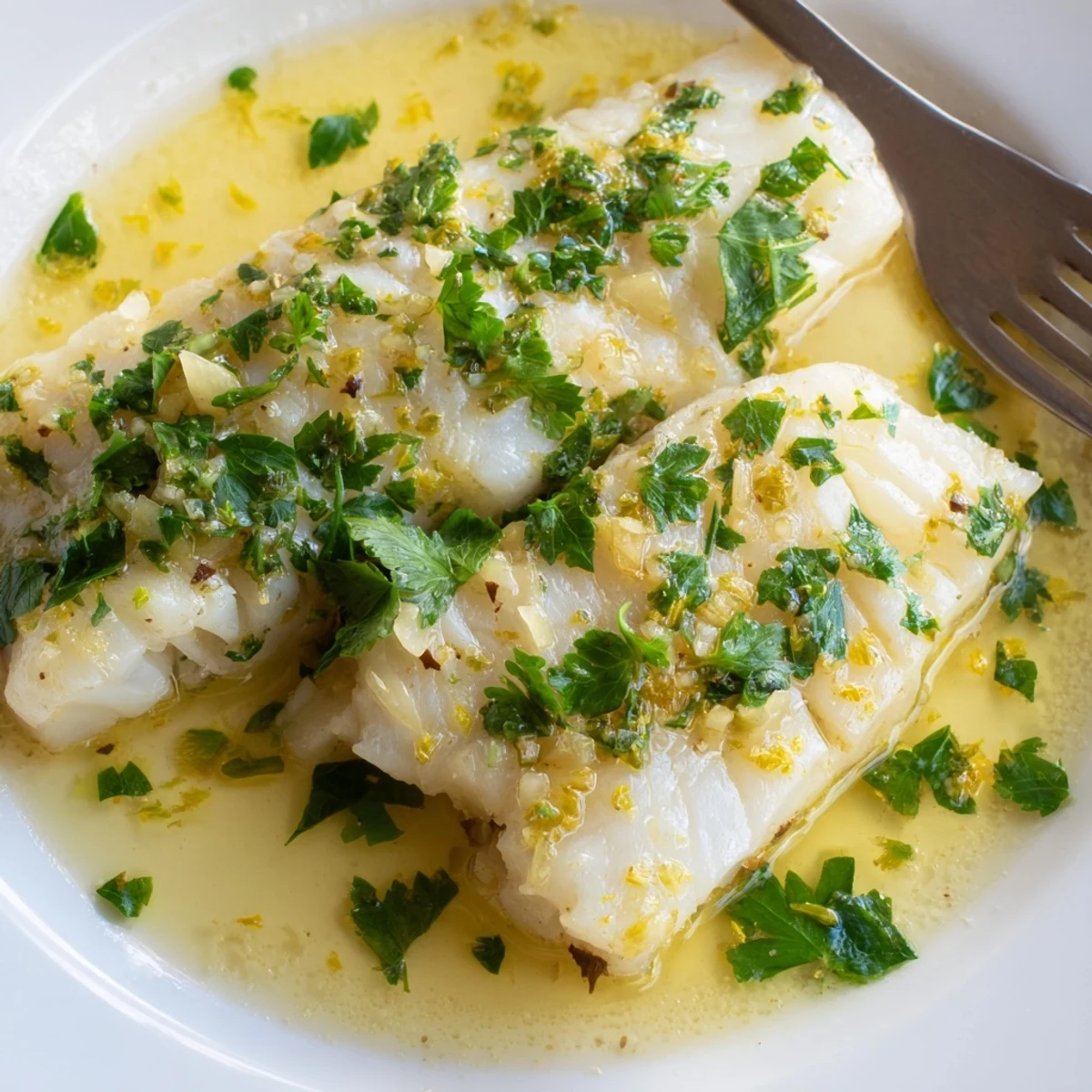 Flaky white fish simmering in rich lemon garlic butter sauce topped with bright lemon wedges and parsley