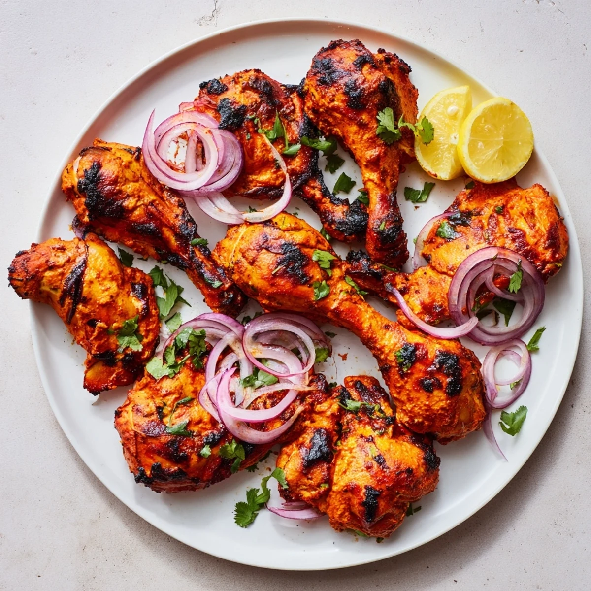 Succulent Tandoori Chicken with vibrant red marinade served alongside sliced red onions and cilantro sprigs