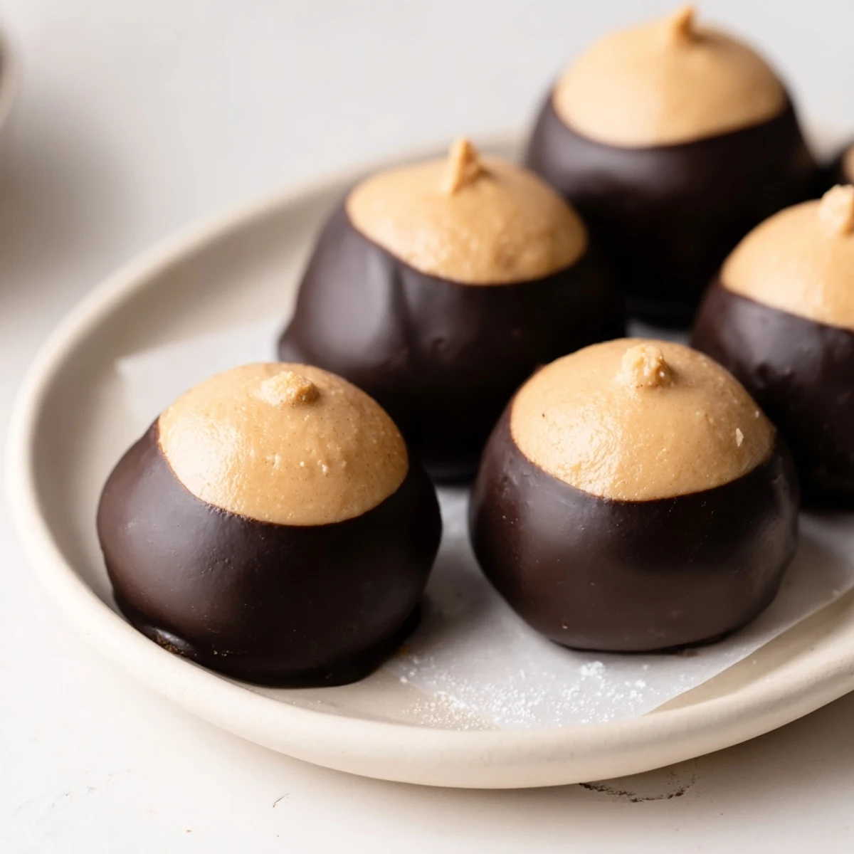 A tray of homemade buckeye cookies features glossy dipped chocolate bottoms and soft peanut butter tops