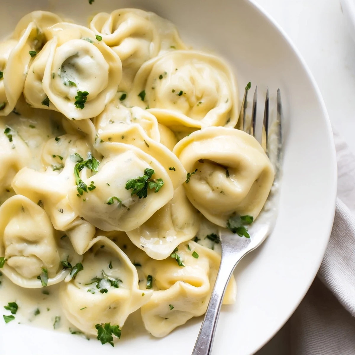 Homemade chicken tortellini bathed in rich butter cream sauce on a white plate
