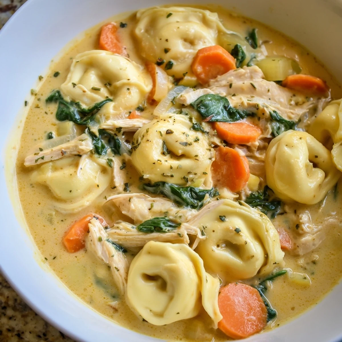Creamy crockpot chicken tortellini in a golden broth with fresh spinach and carrots