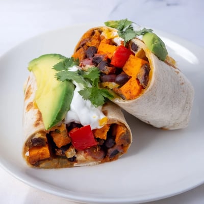 A close-up of a roasted sweet potato and black bean burrito sliced to reveal avocado and melted cheese.