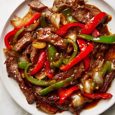A steaming plate of Sizzling Chinese Pepper Steak With Onions rests on a rustic wooden table.
