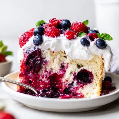 Moist Summer Berry Poke Cake drizzled with vibrant berry sauce on a rustic serving plate