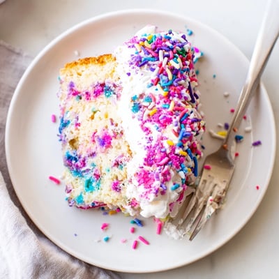 Colorful unicorn poke cake in a baking dish topped with sprinkles and Cool Whip