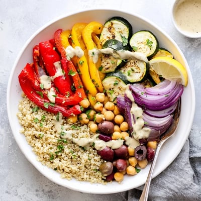 A warm vegan Mediterranean roasted vegetables bowl topped with fresh parsley, kalamata olives, and a lemon wedge.